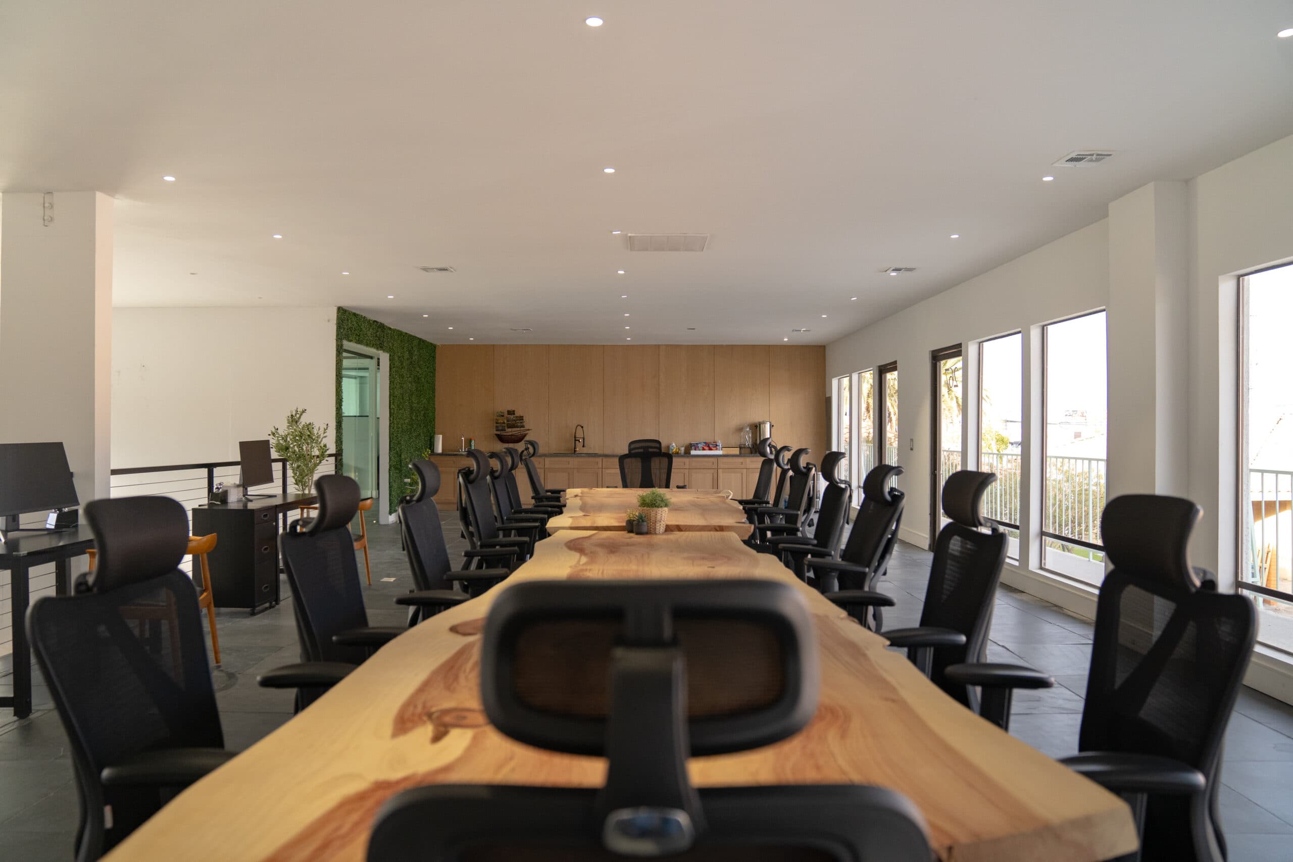 Long live-edge wood conference table with black mesh chairs, a wood-paneled kitchenette and a living green wall