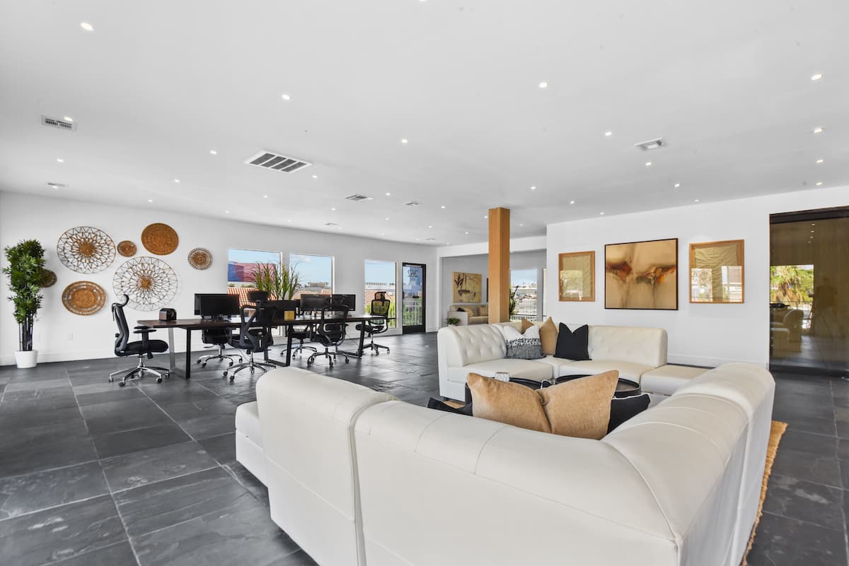 Lounge with a white leather sectional, workstations and woven wall art on slate tile floors
