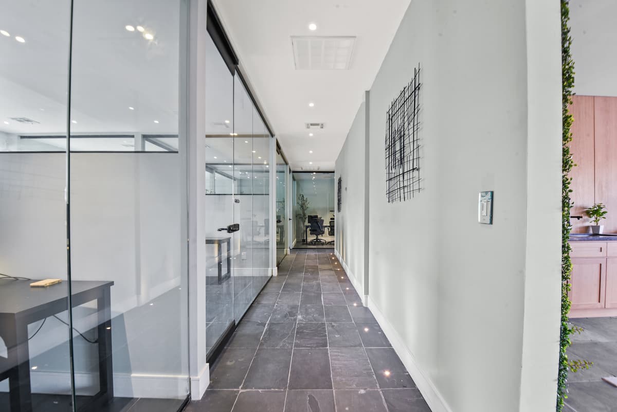 Hallway lined with glass-walled private offices, a slate tile floor and wire wall art