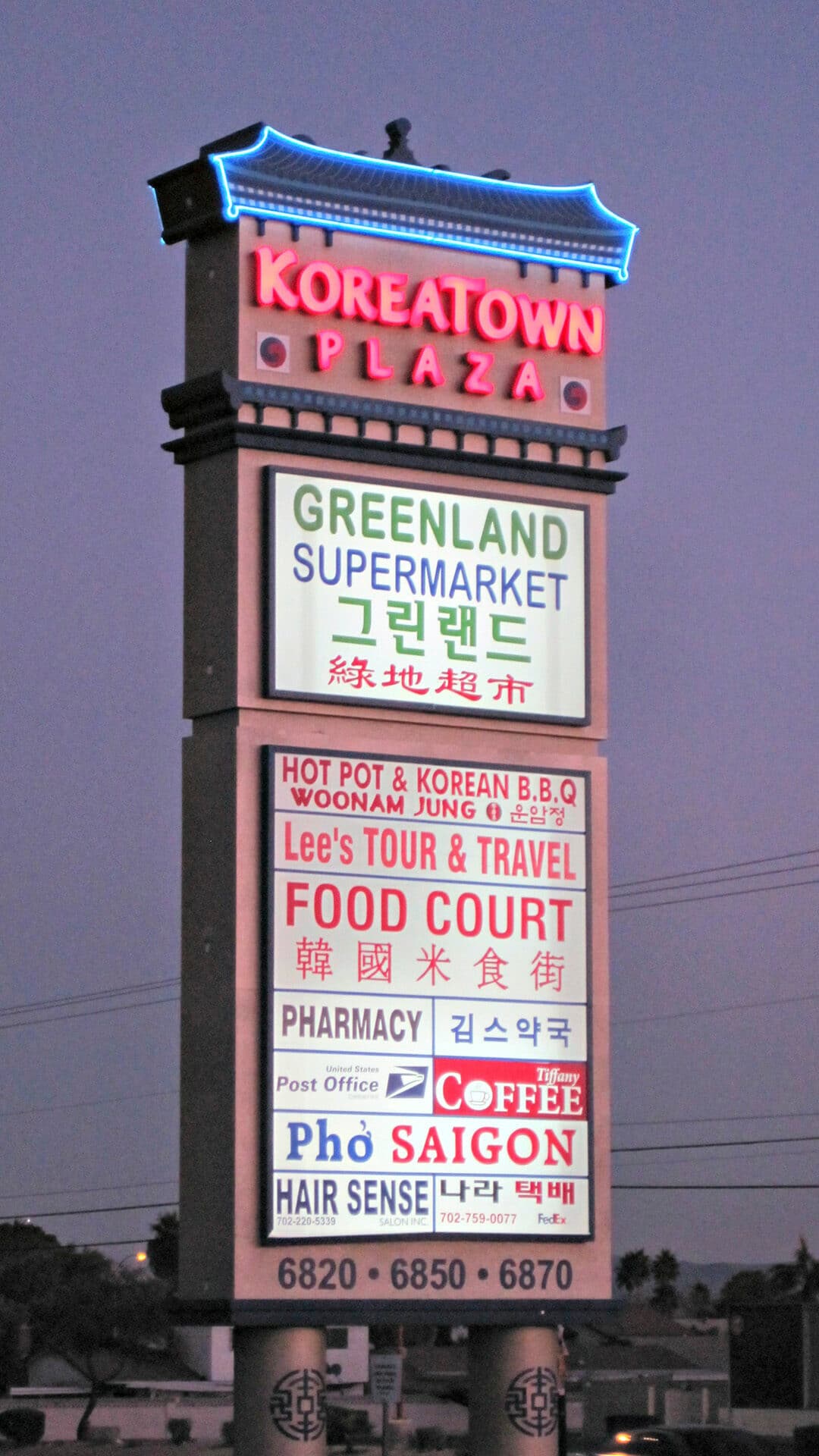 Koreatown Plaza pylon sign at dusk listing Greenland Supermarket, restaurants, a pharmacy and a post office