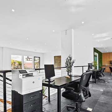 Open desks with monitors and a printer on the mezzanine, overlooking the lounge below